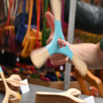 eine Hand dreht auf einem Finger einen Bumerang aus Holz, im Hintergrund Taschen und mehr Bumerangs