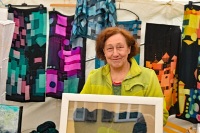 Gerda Müller-Häcker vor dunkler Kleidung mit geometrischen Formen in leuchtenden Farben