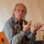 Anselm Ring mit Gitarre hinter verschwommenen kleinen Metallskulpturen