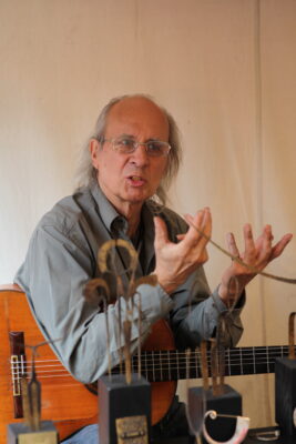 Anselm Ring mit Gitarre hinter verschwommenen kleinen Metallskulpturen
