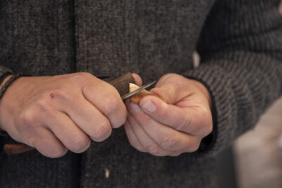 Großaufnahme zweier Hände, die an einem kleinen Stück Holz schnitzen